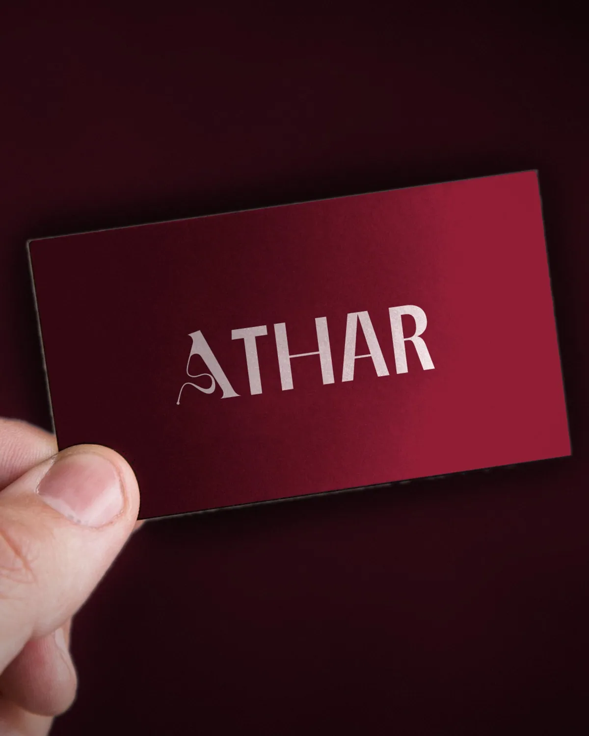 Athar business card in crimson, held up in a hand