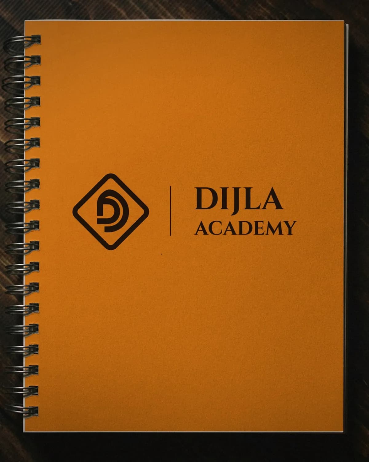 Orange Dijla Academy notebook on a dark wooden desk