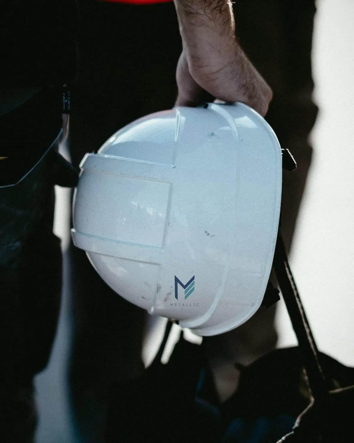 Metallic logo on a white hard hat carried by a worker